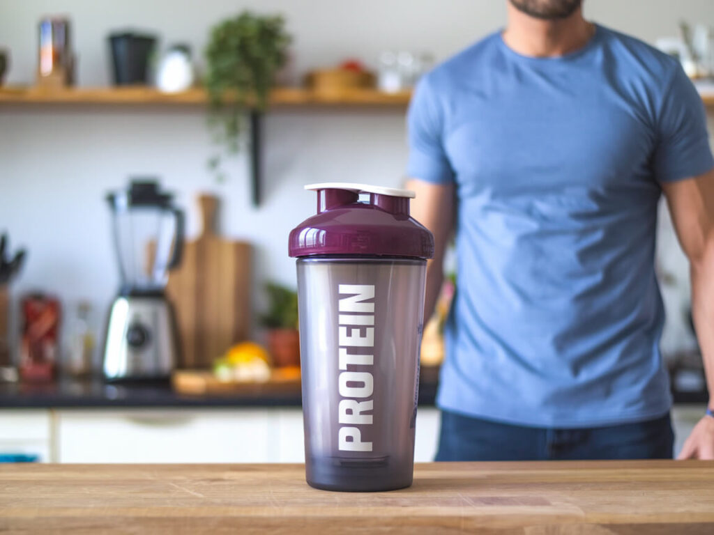 protein shaker bottle with muscular man and kitchen on the background