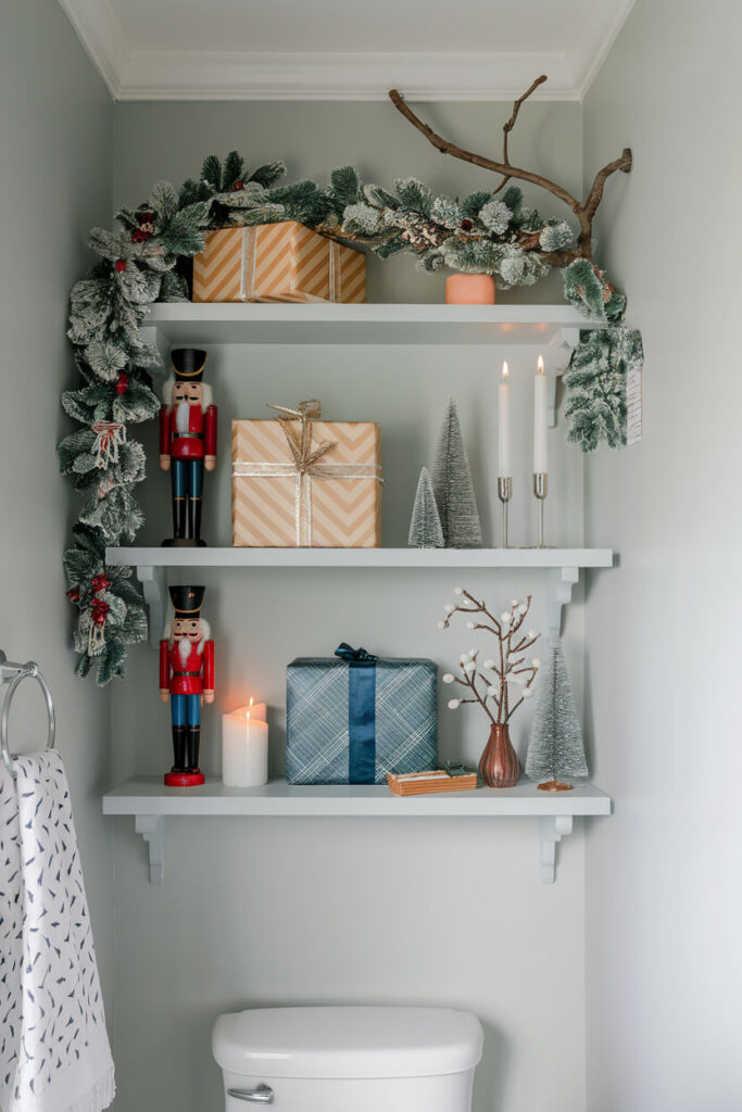 a set of white shelves above toilet with holiday decorations gift boxes, nutcrackers, LED candles, faux garland