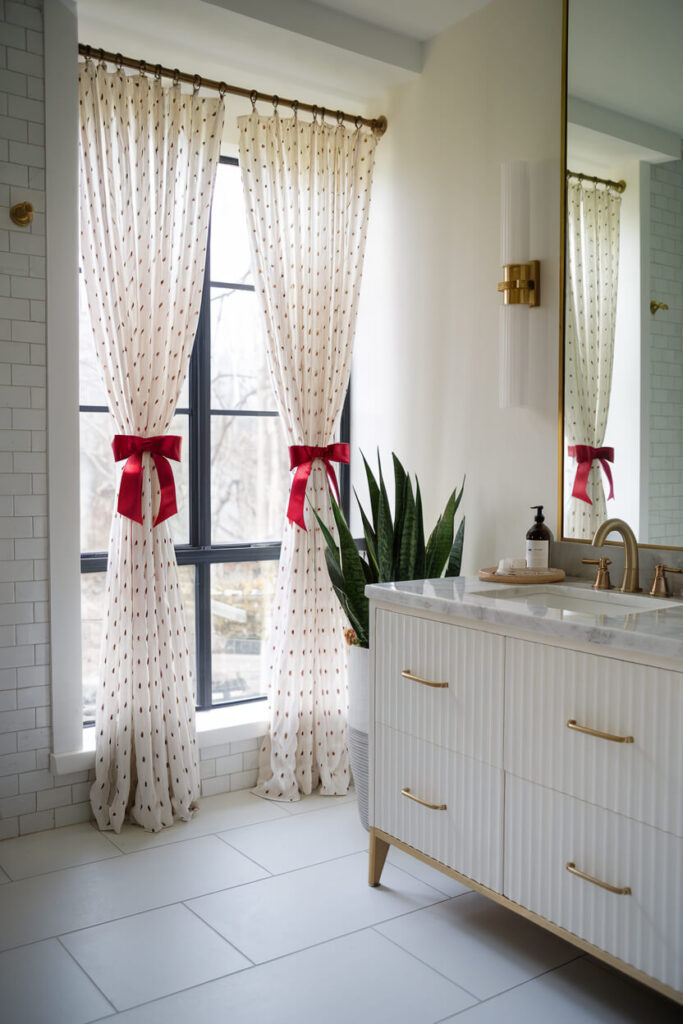 bathroom features a white and gold theme with red ribbons as curtain tiebacks Christmas decor idea