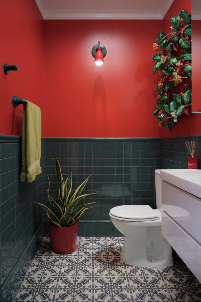 bathroom features a dominant red wall and gray tile adorned with green color items for Christmas palette