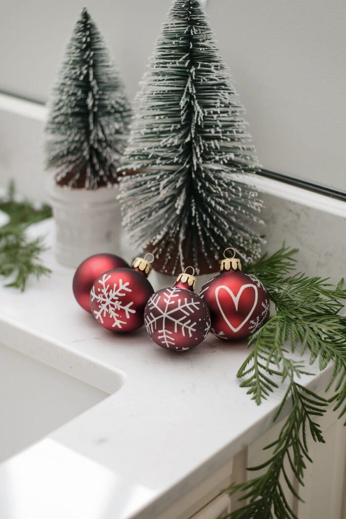 red seasonal ornaments on the white bathroom vanity top, desktop faux mini Christmas trees