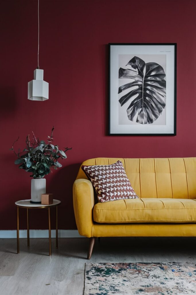 modern yellow couch with beautiful sidetable, maroon wall and decorative pillow, leaf wall art