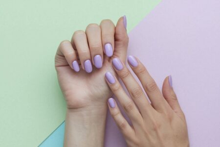 female hands with lilac manicure, pastel background in green and light pink colors