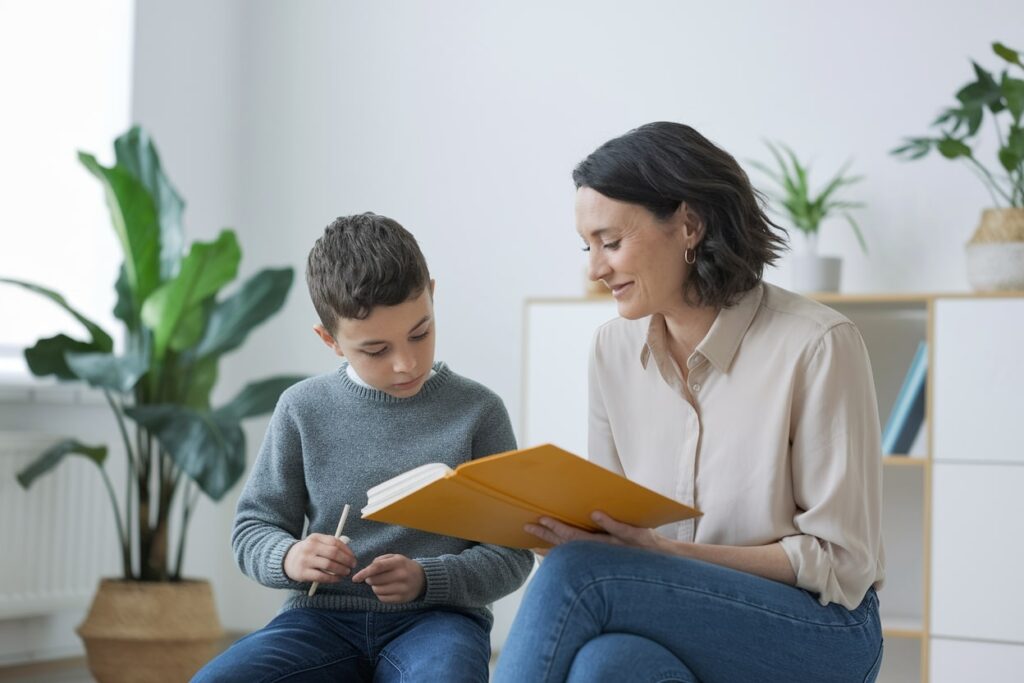 female tutor in a beige shirt and jeans sitting next to a boy student in a gray sweater
