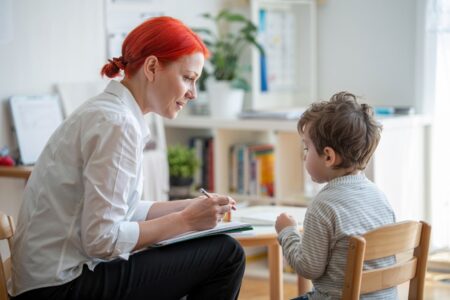 redhead female tutor in a white shirt sitting in the light room with a young boy