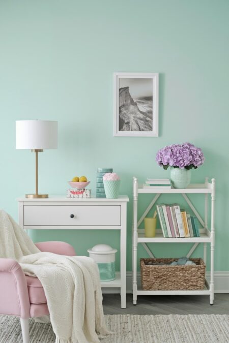 white console table, pastel pink chair, soft green wall. White, green, and purple summer decor, books