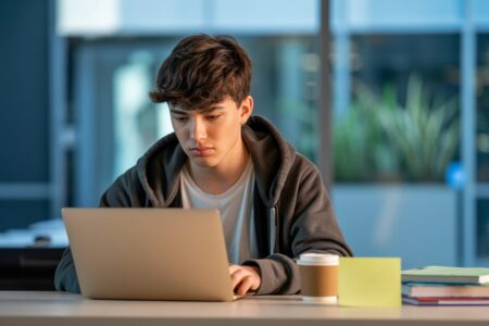 a teen guy in a gray hoodie working on a laptop