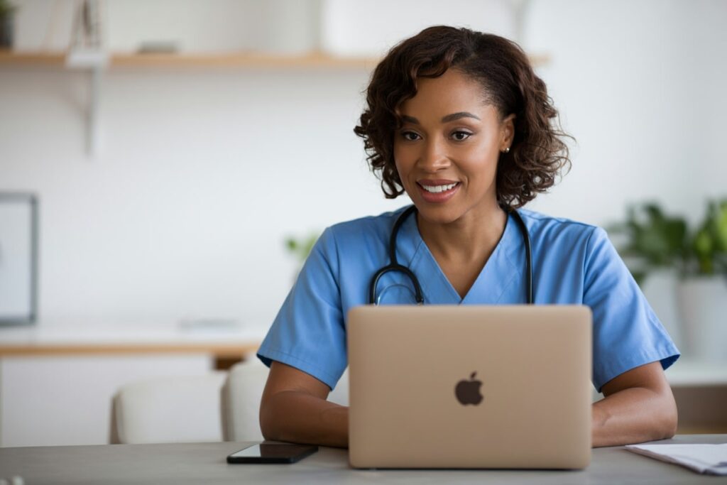 black nurse in a blue scrub working on a laptop