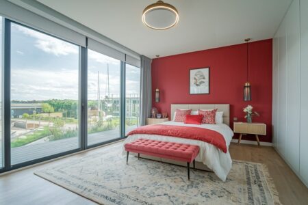 modern bedroom with red accent wall and decor, large windows