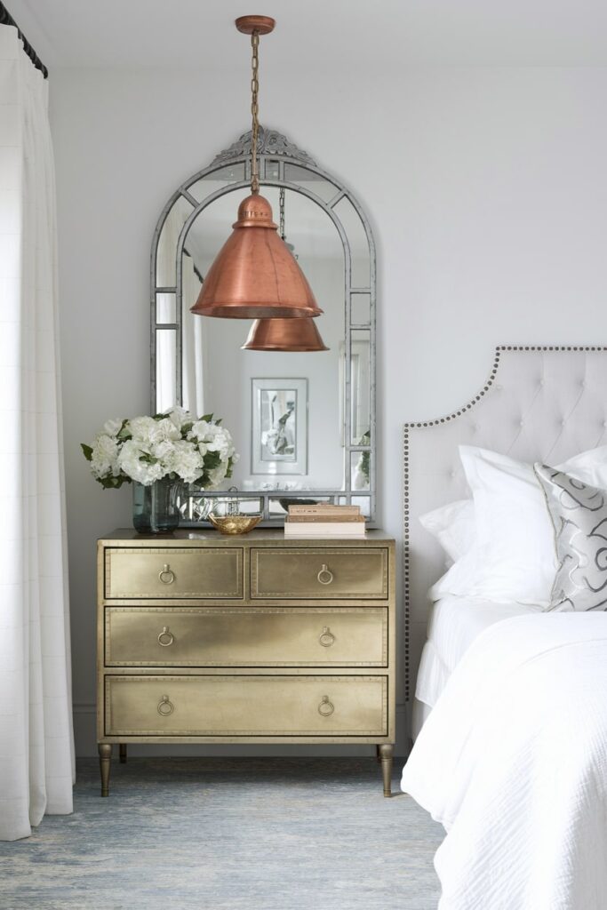 white bedroom with copper pendant light, brass dresser as a nightstand