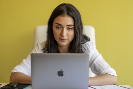 young female in a white blouse working on laptop, white chair, yellow background