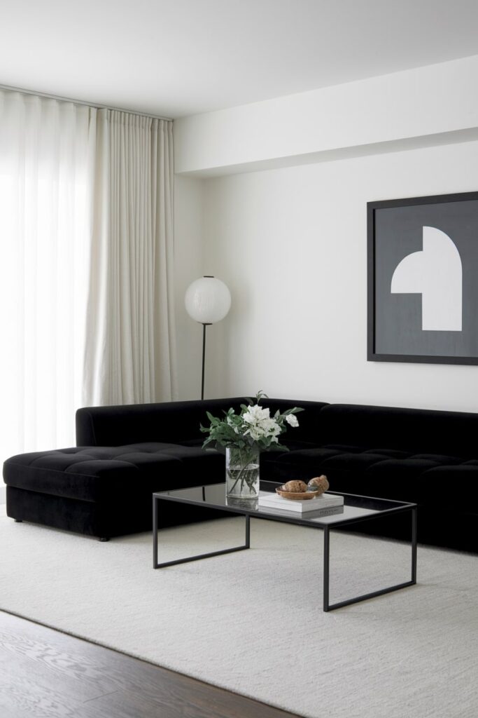 minimalist living room with white walls, black sectional sofa, glass coffee table, and black artwork