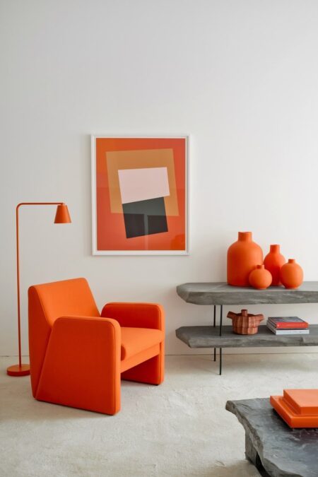 minimalist living room with white walls, orange accent chair, abstract art, and collection of orange ceramic vases