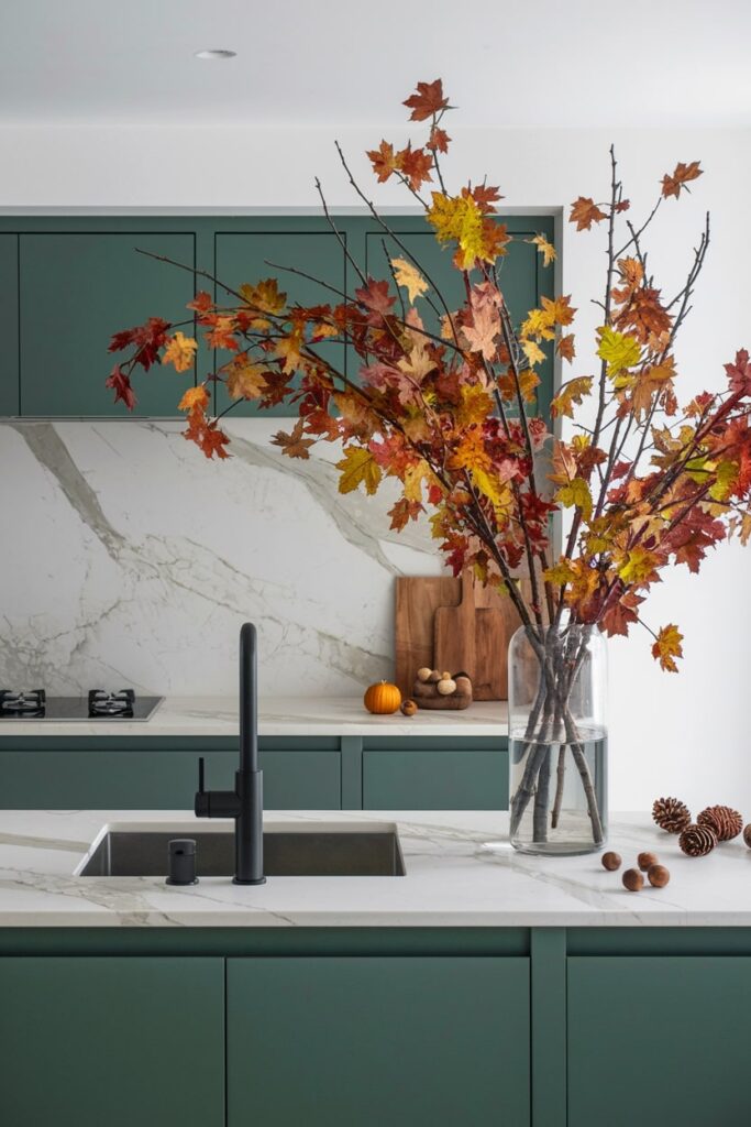modern green kitchen with marble backsplash and island, branches with autumn leaves in a tall glass vase as fall kitchen decor