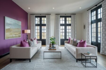 modern living room with purple accent wall and pillows, white furniture, black windows