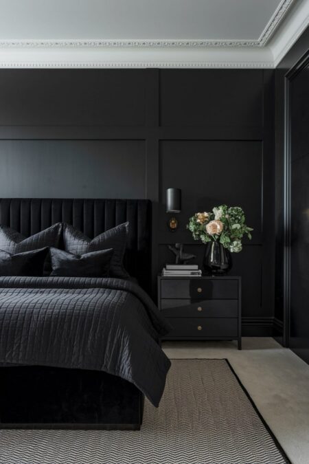 all-black monochromatic bedroom with velvet headboard, glossy nightstand and vase