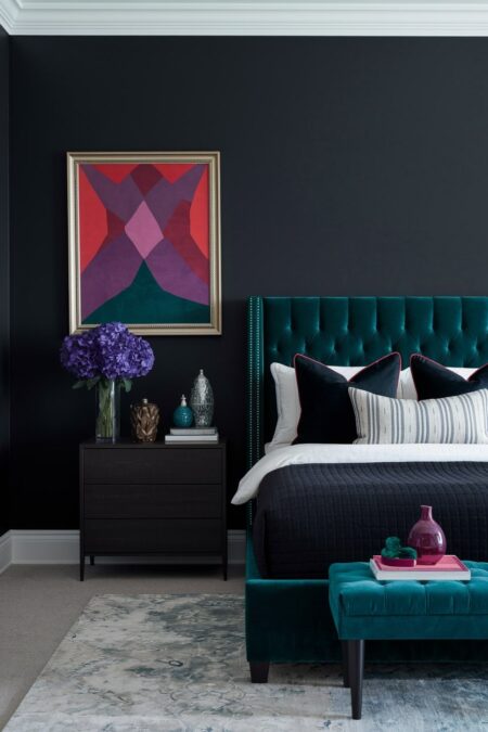 dark bedroom with black walls, jewel tone accents in decor, emerald bed and bench