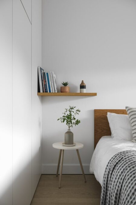 light minimalist bedroom with a single wood floating shelf and white built-in wardrobe