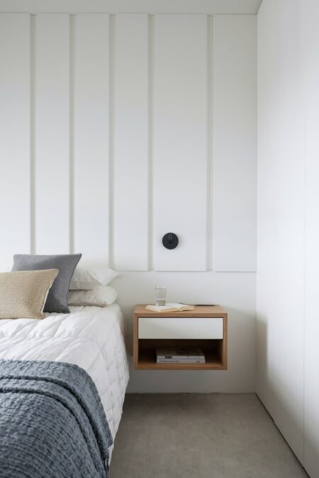 light minimalist bedroom with white wall panels, floating nightstand, and black micro wall sconce
