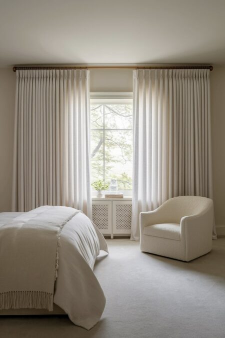 light neutral bedroom with sheer, billowy curtains, and white armchair