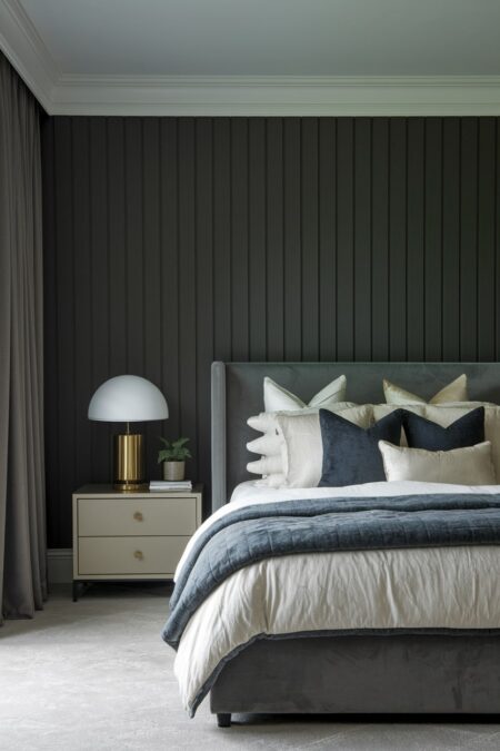 luxury bedroom with dark gray vertical wall panels, gray velvet bed, and gold table lamp