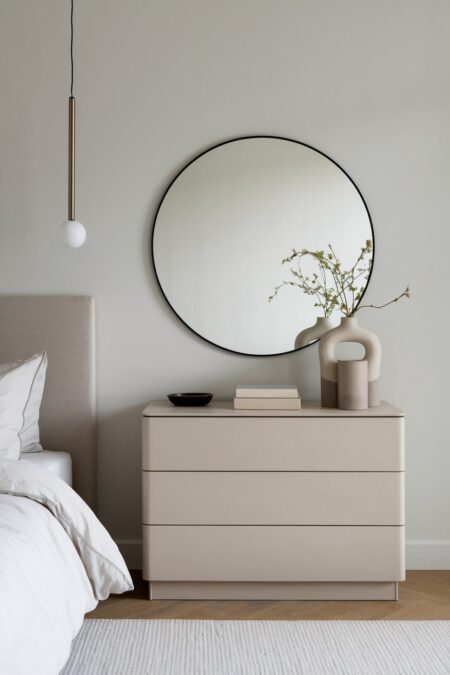 minimalist bedroom with focus on shape, round mirror, rectangular dresser, and spherical pendant light