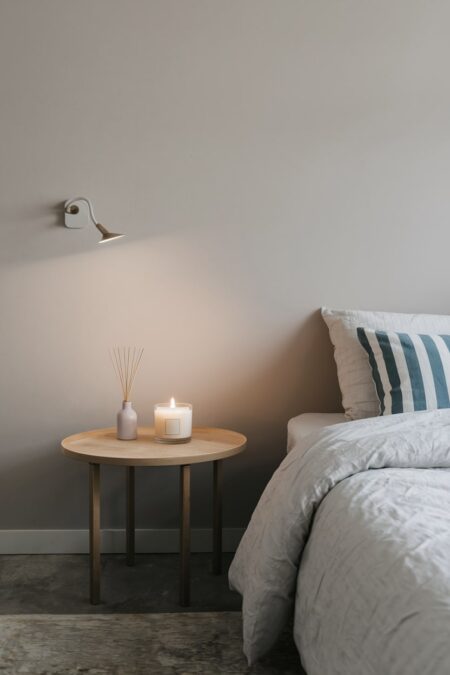 minimalist bedroom with light gray wall, reed diffuser and scented candle on the bedside table