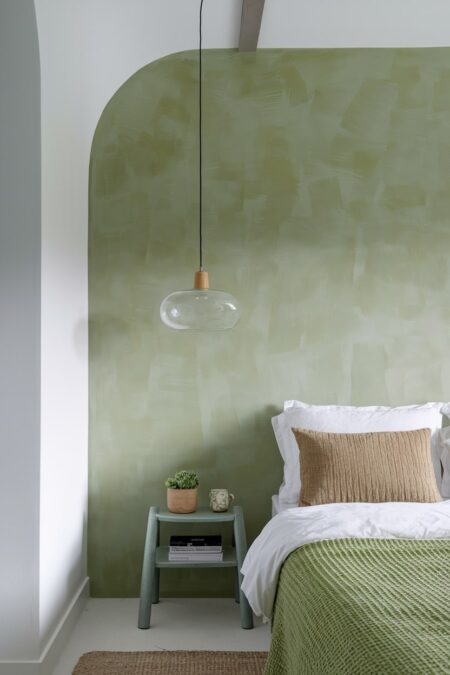 modern bedroom with limewashed sage green wall behind the bed