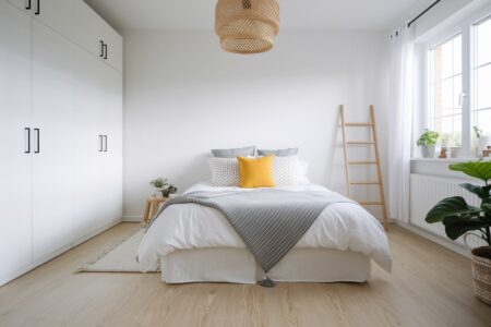 Scandinavian bedroom with a yellow accent pillow, striped black and white blanket, and wooden ladder