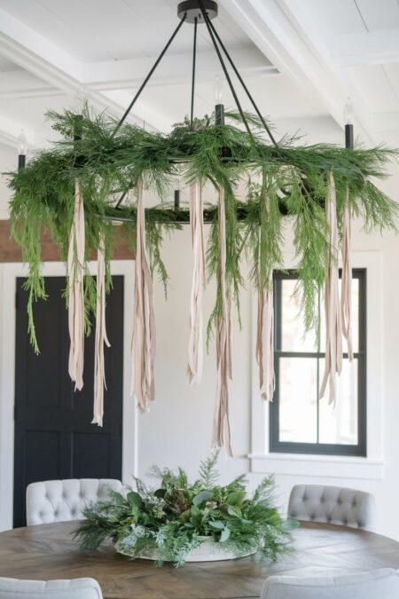 chandelier with evergreen branches and cascading ribbons above dining table as Christmas decor