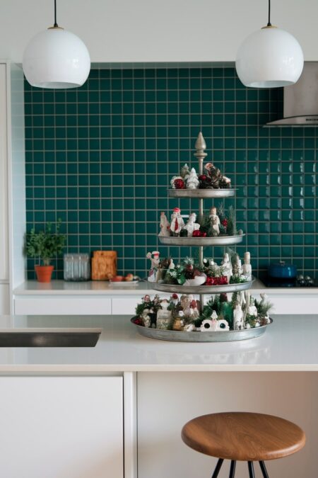 modern white kitchen with green backsplash and kitchen island with multi-tiered tray decorated with a mix of Christmas decor