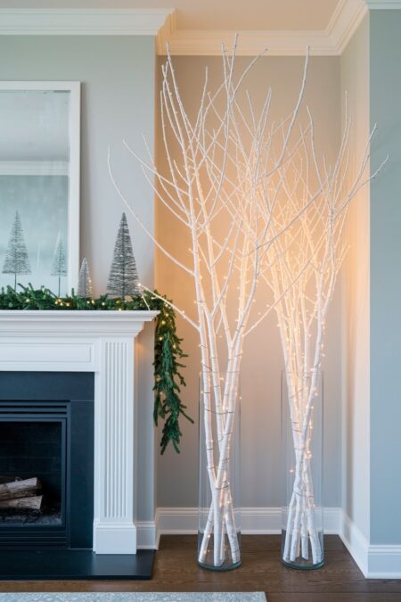 white illuminated branches in tall glass vases near fireplace as Christmas decor