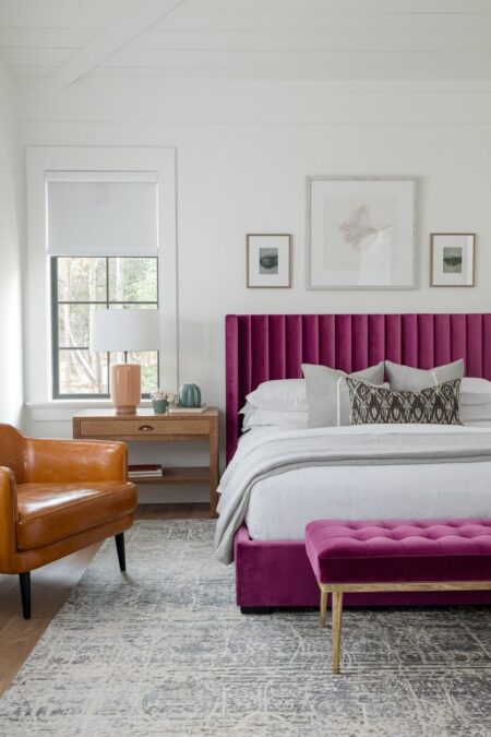 white master bedroom with berry color bed frame and bed bench, leather armchair