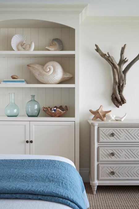 beach bedroom has a cream built-in storage with beach finds (shells and pieces of sea glass) and wall mounted driftwood