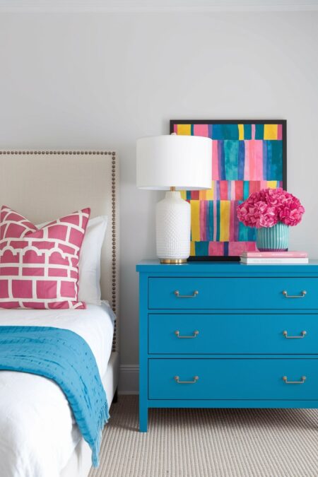 bedroom with a white wall, blue dresser, colorful decor, and cream upholstered headboard