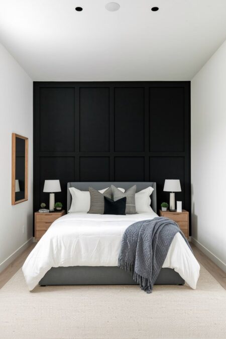 black and white bedroom has a black accent wall with board and batten, white bedding and table lamps, gray bed frame