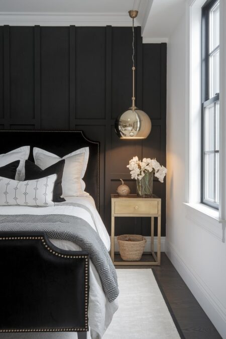 black and white bedroom has a black accent wall with panelling, polished metallic pendant light, and a brass nightstand