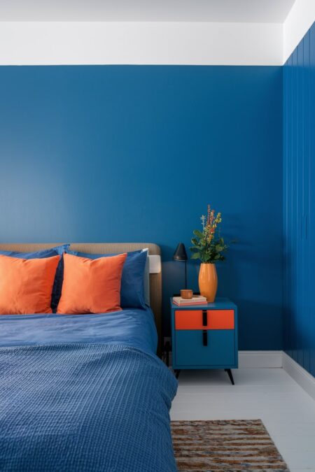 blue bedroom with orange accent pillows and a vase, white flooring