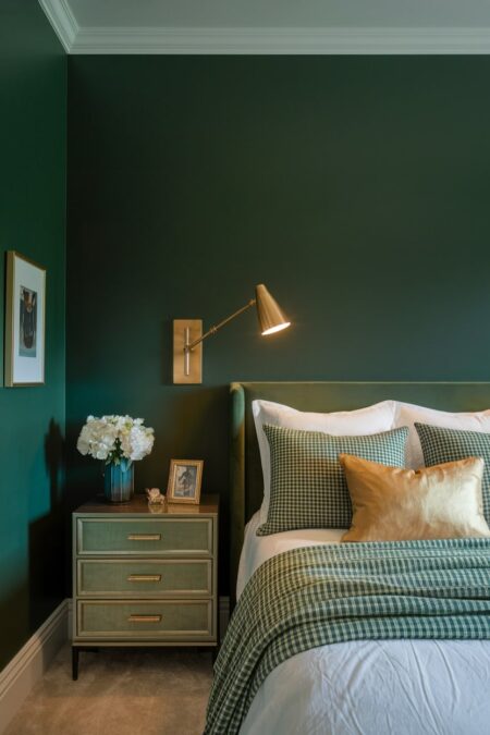 dark green bedroom with velvet headboard and a gold articulated wall sconce
