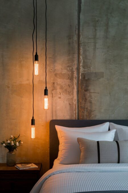 industrial bedroom with a concrete wall, black pendant lights with long cords and Edison bulbs