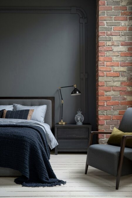 industrial bedroom with a gray accent wall, bedding and armchair with olive green decorative pillow, exposed brick wall