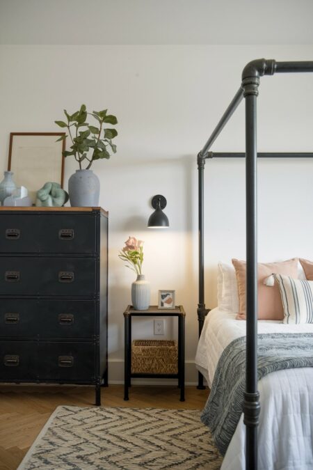 industrial bedroom with white walls, DIY black pipe bedside table and bed frame, black wall sconce and dresser