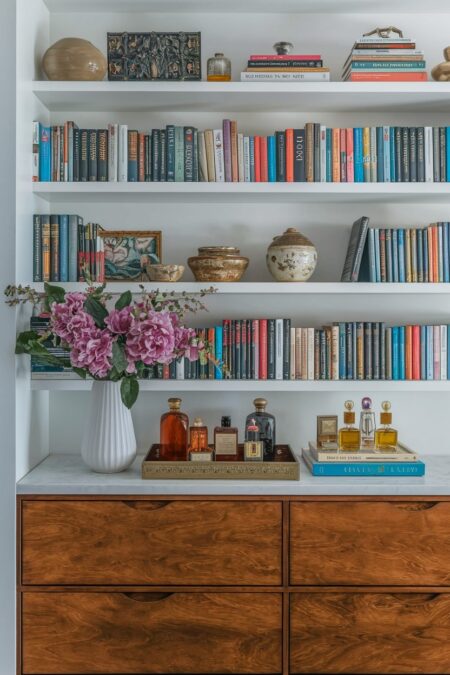 maximalist interior has a dresser with wooden drawers, books on floating shelves, decorative tray with perfume bottles