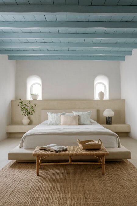 Mediterranean bedroom with a light upholstered low-profile platform bed, jute rug, and exposed beam ceiling painted in light blue color