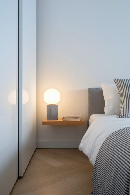 minimalist bedroom with white walls, wooden floating shelf as nighstand with a sphere table lamp