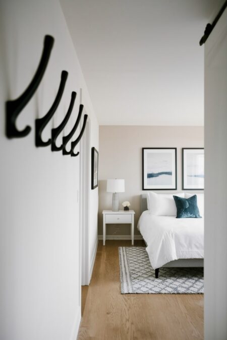modern guest room with white bedding and black wall hooks near the door