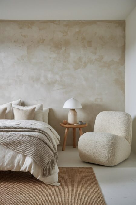 neutral Japandi bedroom with limewashed walls, a soft boucle accent chair, a jute rug, and a ceramic lamp base