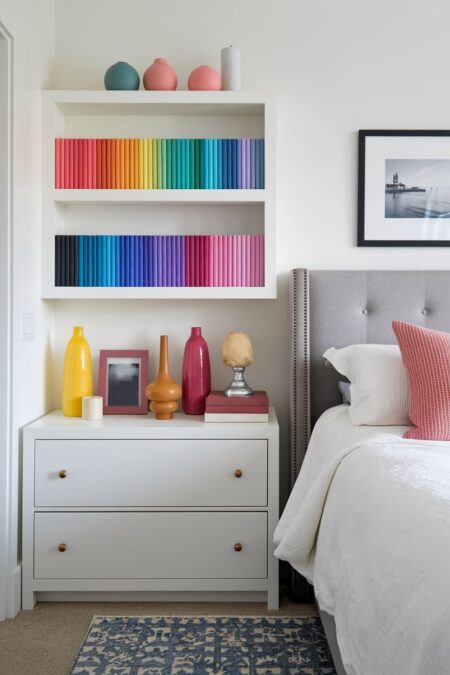 white bedroom with a white nightstand and collection of books in rainbow order on the white floating shelves