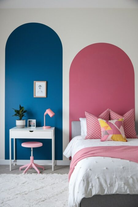 girls' bedroom with color blocking. A painted bold pink arch behind the bed and blue arch behind the desk