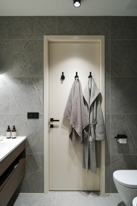 modern bathroom with black hooks on the cream door and gray tile